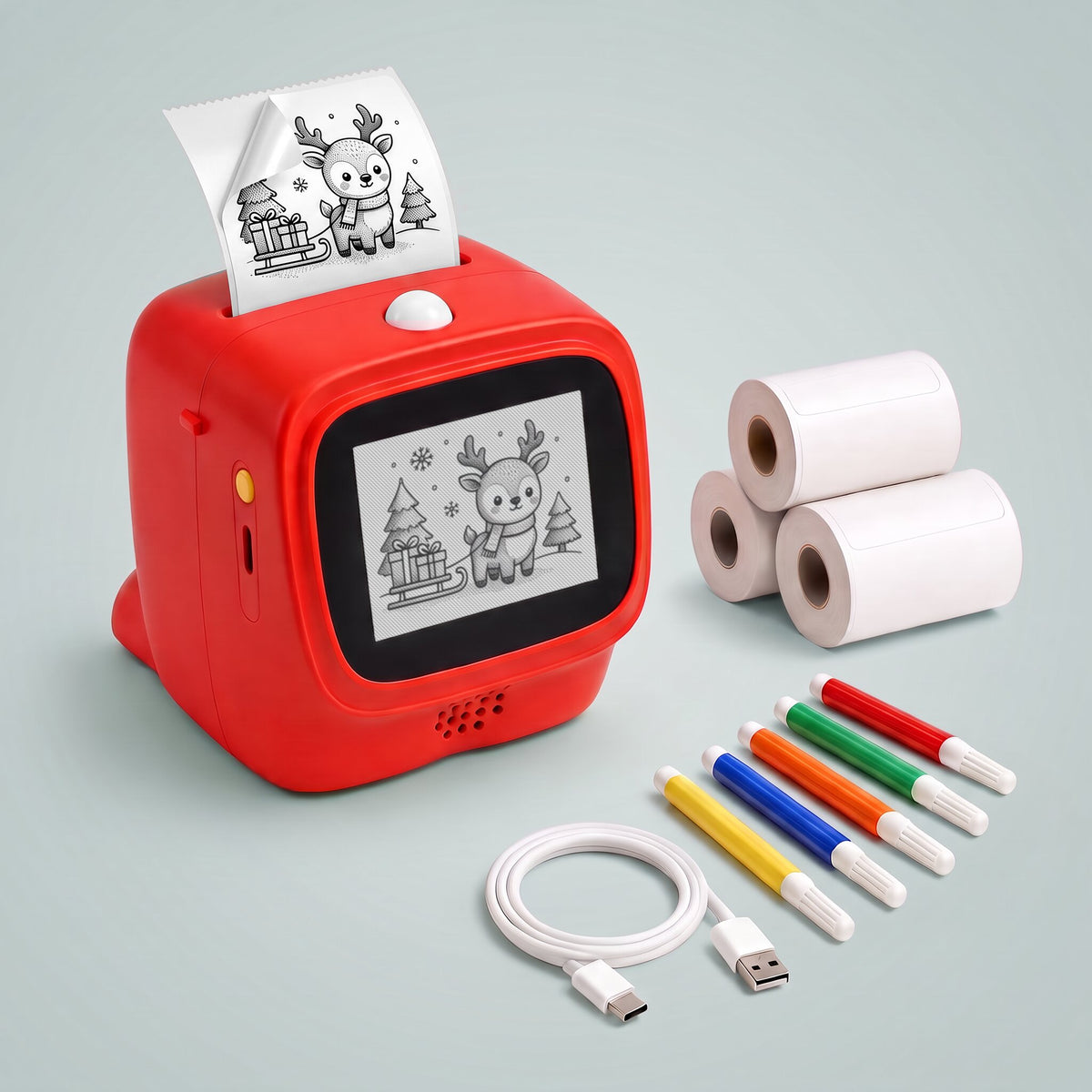 red talkbox AI voice sticker printer with a reindeer drawing printed on continuous peel-off label tape coming out of the top and on its screen, beside three label rolls, five markers and a USB cable